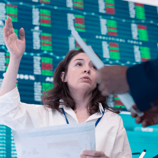 A professional woman standing in front of a large screen displaying stock charts and financial data, explaining market trends with gestures, wearing business attire in a modern office setting
